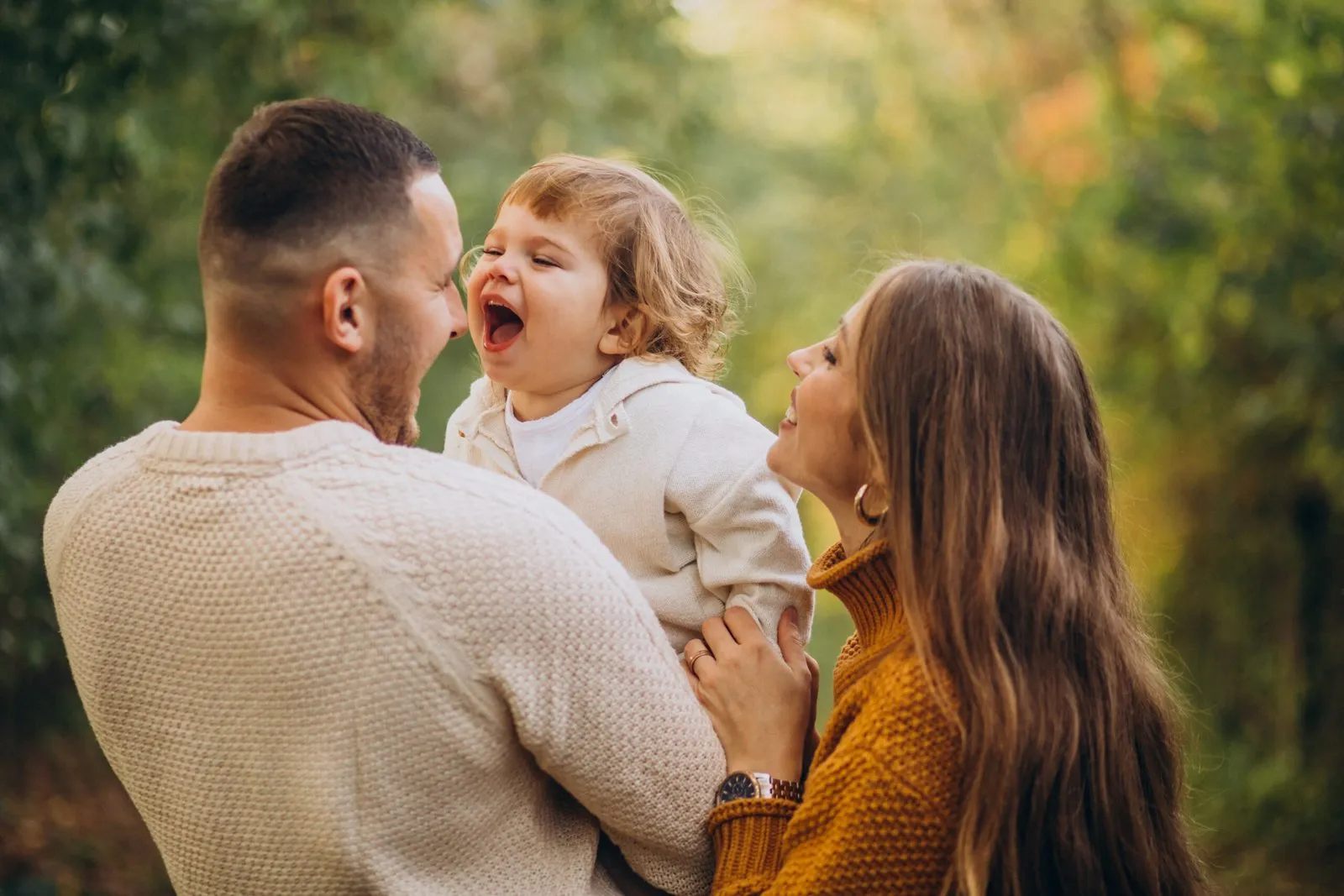 Pai e mãe sorrindo com o filho pequeno no colo, ao ar livre